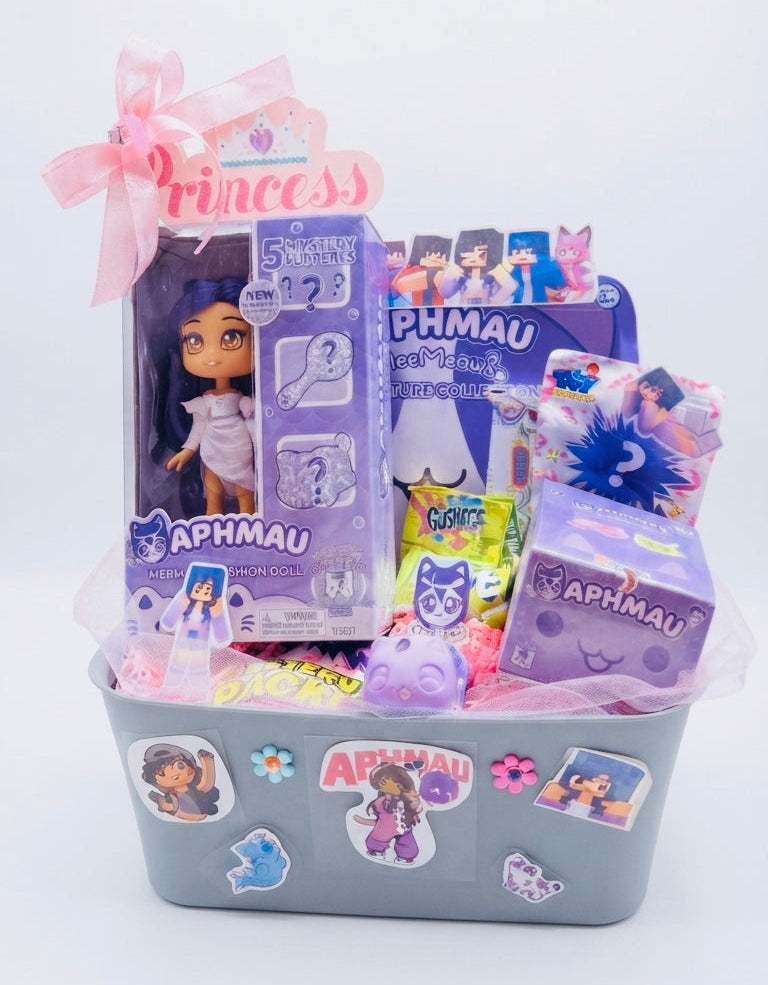 A themed toy and mystery box gift basket featuring the Aphmau brand, including a boxed doll, various colorful mystery packages, and a pink ribbon bow, all arranged in a gray plastic basket decorated with stickers.